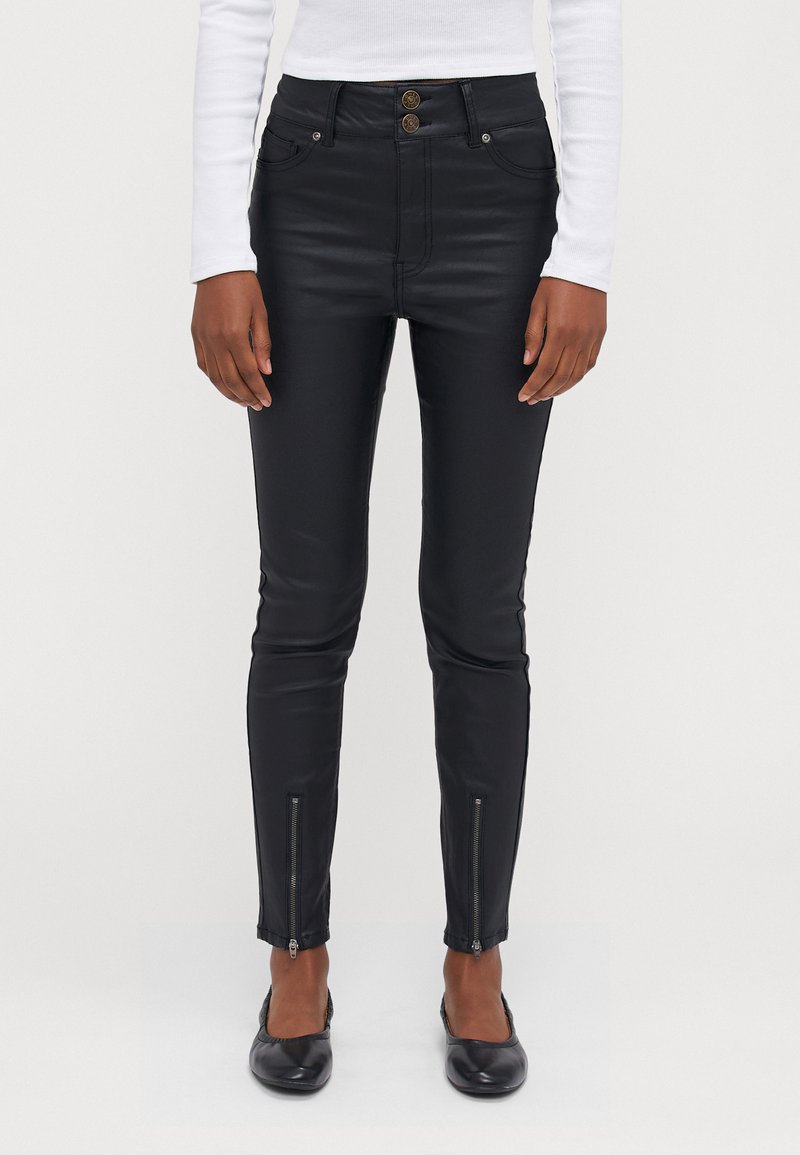Zwarte faux leren broek met een hoge taille, dubbele knoopsluiting, voorzakken en ritsen bij de enkels. Glad oppervlak en aansluitend ontwerp.