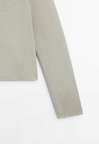 Vaaleanharmaa neulepaita, jossa on teksturoitu kangas, pitkät hihat ja resorireuna. Yksinkertainen malli ilman lisäkuvioita tai koristeita.