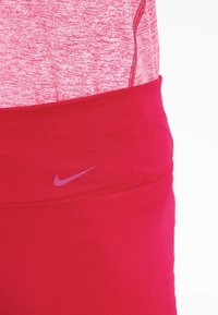 Leggings Nike rouges avec une texture lisse et extensible. Comprend une large ceinture avec un petit logo violet et une coupe ajustée.