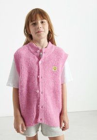 Roza pletena brezrokavnik z teksturiranim vzorcem, ki ima stoječ ovratnik, pet gumbov in majhno rumeno logotip na prsih.