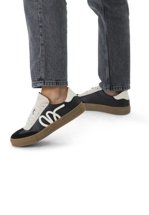 Black and white sneakers with a gum sole, featuring a smooth finish and prominent white logo design across the lateral side.