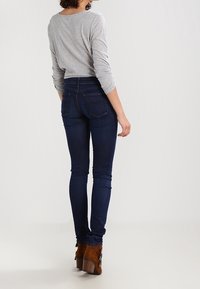 Jeans ajustados de color azul oscuro con cintura alta, combinados con una camiseta de manga larga gris claro y botas de tobillo marrones con un tacón robusto.