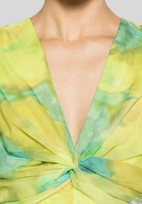 Top a scollo a V con dettaglio annodato al centro. Realizzato in tessuto leggero nelle tonalità di verde e giallo, con una superficie liscia.