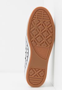 Semelle d'une basket Converse All Star en noir et blanc avec une semelle extérieure en caoutchouc gomme texturée présentant un motif géométrique et le logo de la marque.