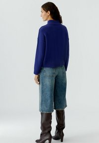 Blauwe gebreide coltrui, cropped model, gecombineerd met lichtblauwe wijde jeans en donkerbruine kniehoge laarzen. Zachte textuur door het geheel.