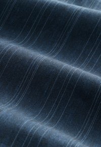 Tissu bleu foncé avec des fines rayures blanches verticales uniformément espacées, délicatement plié pour montrer la texture et le détail du tissage.