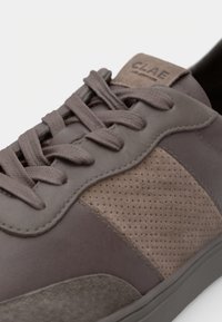 Baskets en cuir marron présentant un panneau latéral texturé, des accents perforés et un design traditionnel à lacets avec une étiquette logo sur le talon.