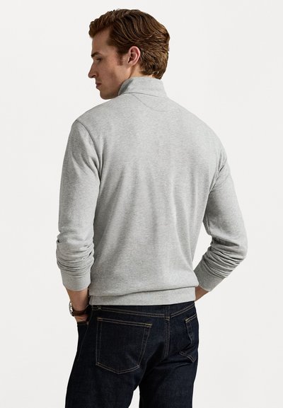 Lys grå, langermet genser med høye krage. Har ribbestrikkede mansjetter og nedre kant. Parret med mørk denim jeans. Glatt tekstur.
