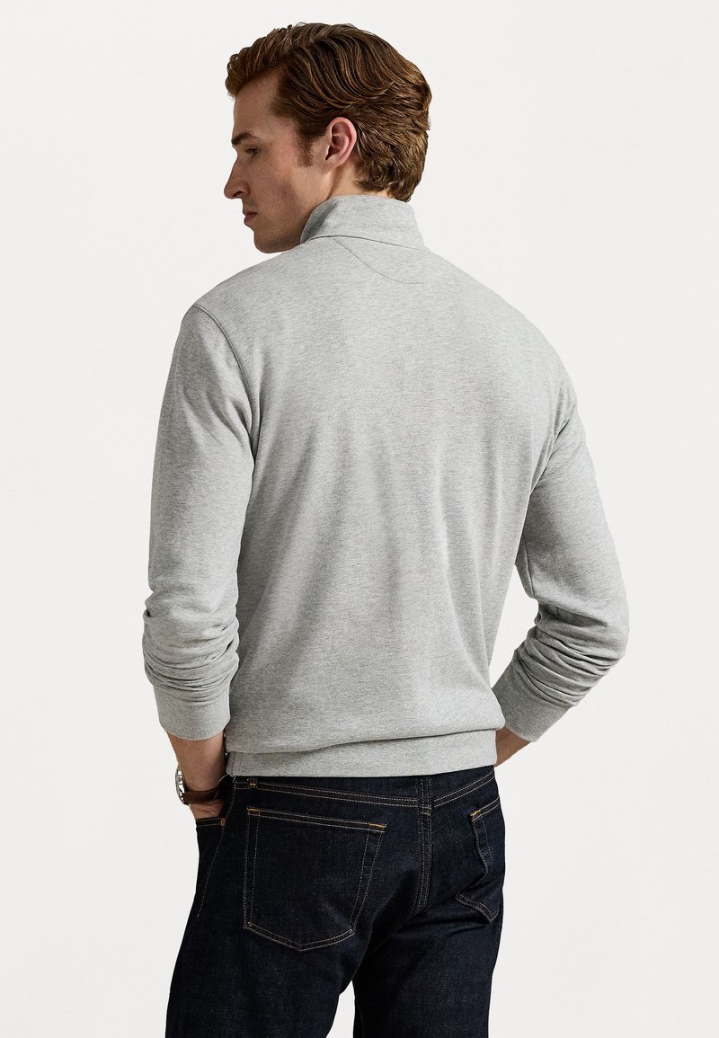 Pullover de manga larga gris claro con cuello alto. Cuenta con puños y dobladillo de canalé. Combinado con jeans de mezclilla oscura. Textura suave.