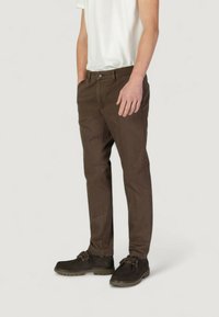 Chino in cotone marrone con vestibilità slim, dotato di chiusura a bottone, tasche laterali e cuciture tono su tono, abbinato a scarpe marroni scure.