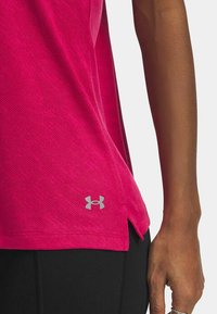 Fuchsia sportshirt van textuurstof, met een zijsplit en een grijze Under Armour-logo nabij de zoom. Zwarte leggings zijn gedeeltelijk zichtbaar.