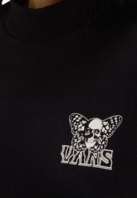 Collo nero in cotone con una grafica bianca di un teschio integrato con una farfalla sopra il logo "VANS".