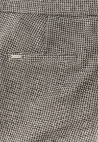 Zbliżenie małej kieszeni z materiału w wzór houndstooth z metalową etykietą z napisem "Street One".
