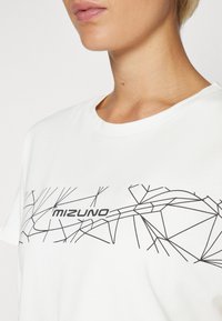 Bijela majica kratkih rukava s crnim geometrijskim uzorkom i natpisom "Mizuno" na prsima. Mekani pamučni materijal.