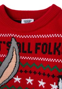 Pull en laine rouge avec le texte "C'est tout, mes amis!", un design de personnage de cartoon, des étoiles blanches et des motifs en zigzag verts.