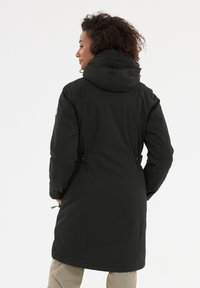 Zwarte lange jas met een capuchon, taille-detail en zijzakken. Glad, waterafstotend materiaal. Achteraanzicht toont de stiksels en stoftextuur.