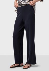 Marinblå vida byxor av mjukt tyg med resår i midjan, i kombination med svarta sandaler med guldkant. 