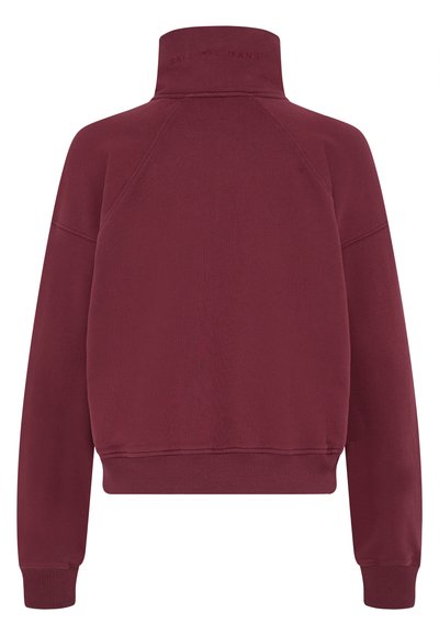 Burgundski pulover s visokim ovratnikom, raglan rokavi ter ribanim robom in manšetami. Mehak teksturiran material z diskretnim logotipom na ovratniku.