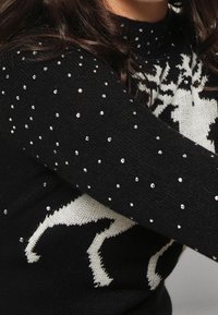Svart tröja med en vit ren-design, prydd med utspridda rhinestones. Stickad textur, med ribbad halsringning.