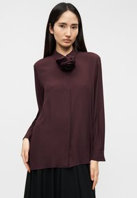 Μπλούζα μακρυμάνικη στο χρώμα του βουργουνδίου με τριαντάφυλλο στη γιακά, με λεία υφή και άνετη εφαρμογή.