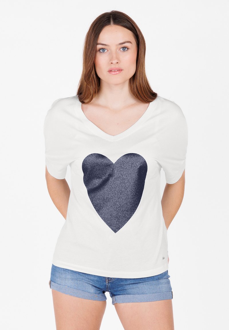 Camiseta blanca de manga corta con un gran gráfico de corazón de purpurina azul marino en el frente, con un diseño de escote en V y textura suave.