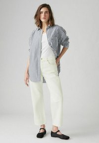 Gestreept overhemd in blauw en wit, witte tanktop, lichtgele wijde jeans en zwarte ballerina's. Eenvoudige, casual outfit.