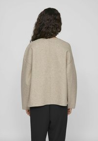 Pull beige surdimensionné avec un col rond, des épaules tombantes et un ourlet droit. Fabriqué en tissu doux et texturé, porté sur un pantalon noir.