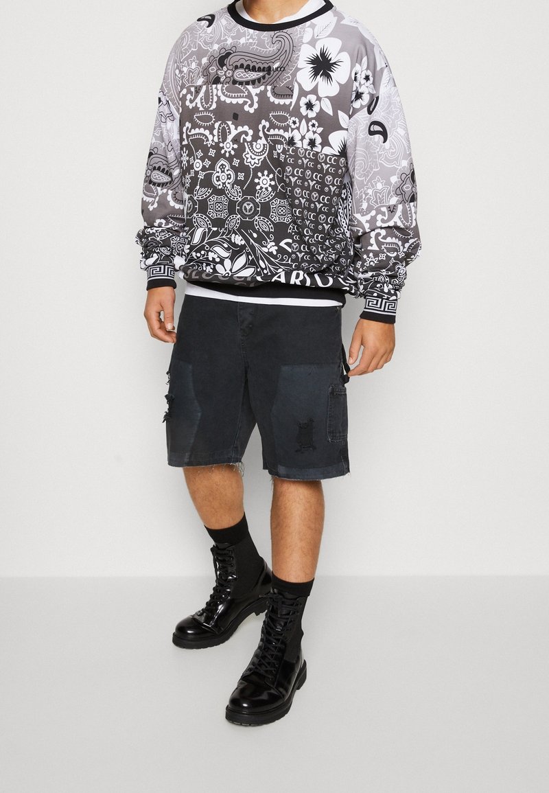 Černobílá mikina s květinovými a paisley vzory, doplněná černými kargo šortkami s třepeným lemem a trhlinami. Černé vojenské boty.