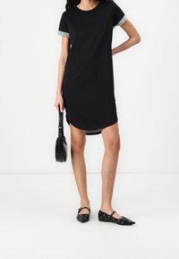 Svart kortärmad klänning med grå manschetter, med rund halsringning och sprund på sidorna. Matchad med svarta platta skor och en rund handväska.