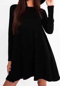 Robe noire à manches longues au fit décontracté, avec un col rond et une jupe évasée, fabriquée en tissu doux à la texture lisse.