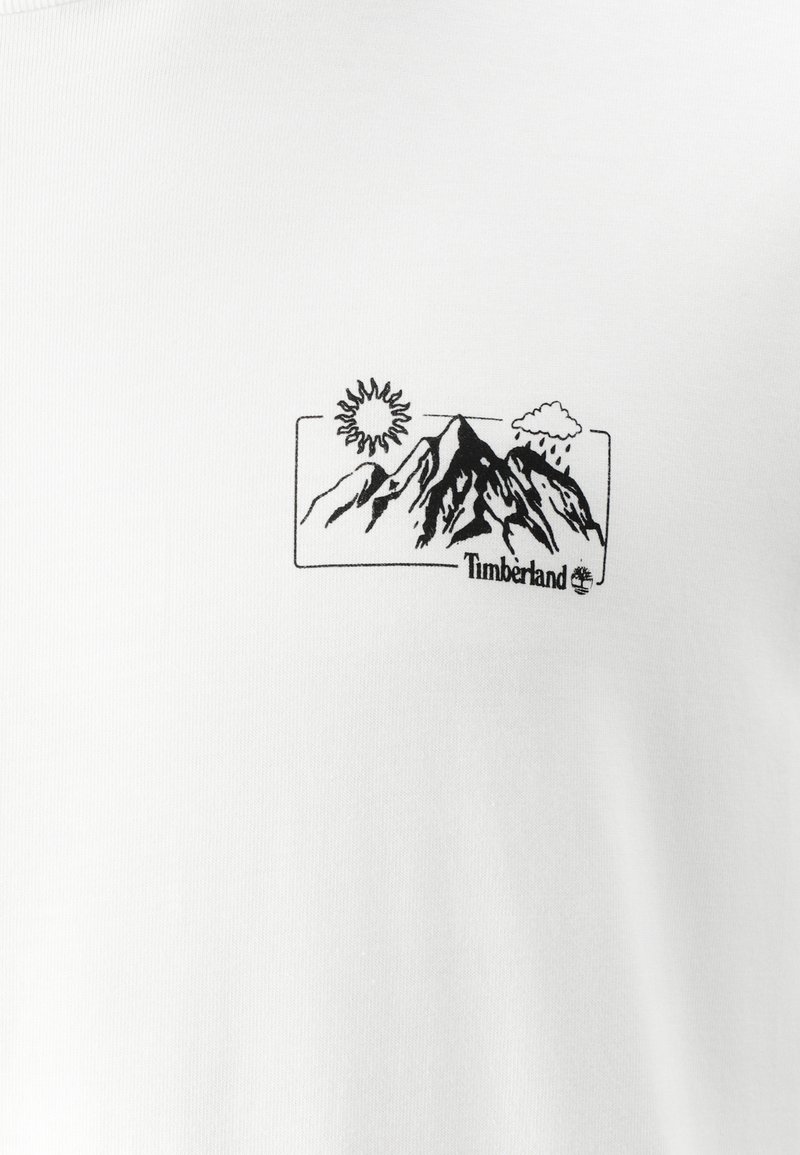 T-shirt en coton blanc avec un graphique noir de montagnes, d'un soleil et de nuages, accompagné du texte "Timberland" en bas.