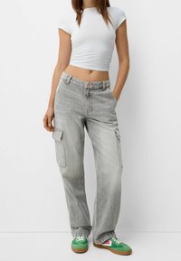 Pantalones cargo gris claro con bolsillos laterales, corte holgado y cinturilla elástica, combinados con un top corto blanco y zapatillas coloridas.