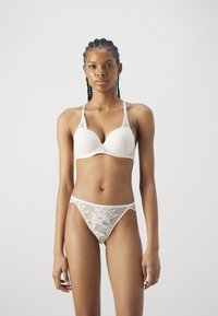 Balta nėriniai liemenėlė su gilia iškirpte ir reguliuojamomis petnešėlėmis, derinama su atitinkamomis nėrinių kelnaitėmis su gėlių raštais.