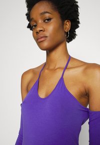 Top roxo com alças, decote profundo em forma de U, feito de um tecido suave e liso, apresentando mangas longas off-shoulder e uma silhueta justa.