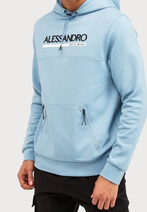 Mand iført lyseblå Alessandro Zavetti Milano hættetrøje med lynlåset frontlomme og sorte snore, kombineret med sorte bukser.