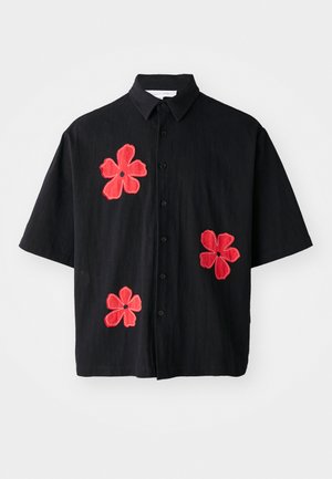 Camisa negra de manga corta con gran bordado floral rojo en la parte delantera, con collar de botones y un corte relajado.