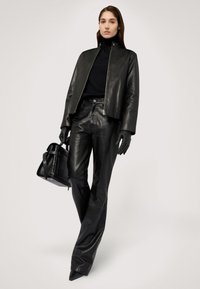 Schwarze, beschneiderte Lederjacke; enganliegender schwarzer Rollkragenpullover; schwarze Lederhose; schwarze Handtasche mit strukturiertem Finish; schwarze Handschuhe; spitze Absatzschuhe.