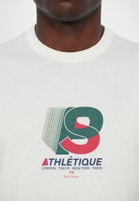 Hvit bomulls T-skjorte med grafisk design; har grønn og rød tekst "ATHLÉTIQUE" og stilisert "S" med bynavn og "PS Paul Smith."