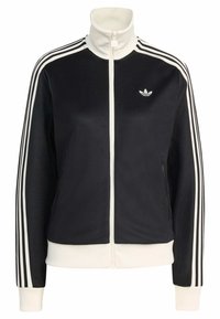 Črna športna jopa z zadrgo in visokim ovratnikom, z belimi črtami na rokavih in belimi rebrastimi manšetami. Na prsih majhen logotip in žepi.