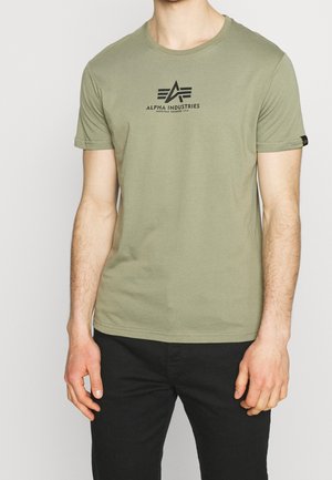 Camiseta verde oliva de algodón, con cuello redondo y mangas cortas. Presenta un logo negro, "ALPHA INDUSTRIES", en la parte delantera.