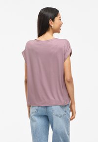 Short-sleeve T-shirt in light mauve, featuring a relaxed fit and rolled sleeves. Paired with high-waisted light wash denim jeans.