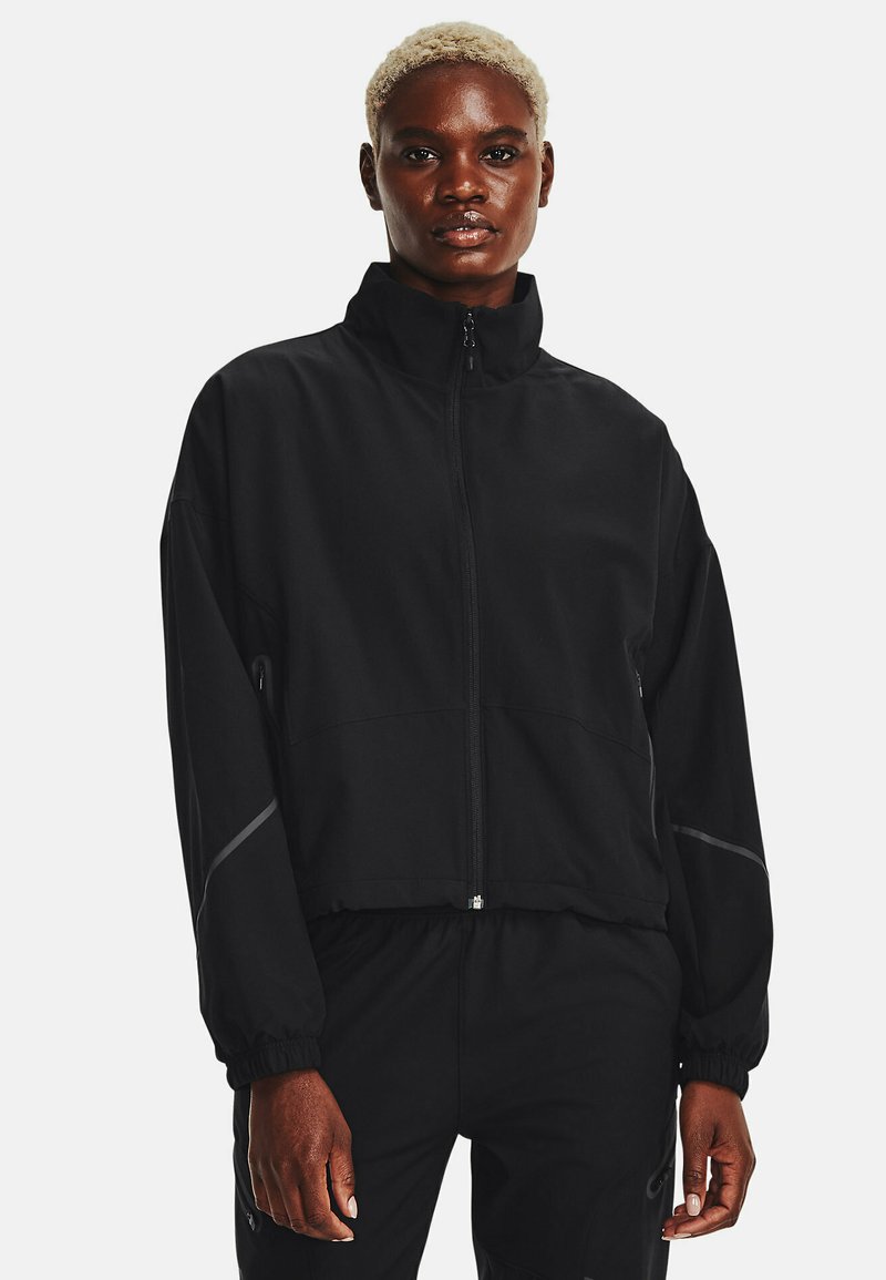 Giacca cropped nera con colletto alto, chiusura con zip e polsini elasticizzati; presenta dettagli riflettenti sulle maniche e una texture liscia.