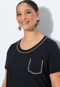 Camiseta negra con cuello redondo adornado con embellishments plateados a lo largo del collar y el bolsillo, mangas cortas, textura suave.