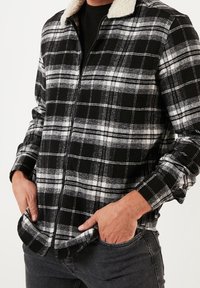 Schwarz-weiß karierte Jacke mit Reißverschluss und weichem cremefarbenem Kragen. Mit langen Ärmeln und Vorderentaschen. Strukturierter Stoff.