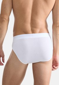 Caleçons en coton blanc avec une texture lisse, une taille élastique et un design minimaliste, présentés de dos.