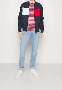 Marine bomberjakke med hvide og røde paneler, ribbede manchetter, parret med en rød og hvid stribet T-shirt og lyseblå jeans, afsluttet med hvide sneakers.