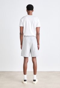 Gray sweat shorts with an elastic waistband, paired with a white T-shirt. Features a back pocket, loose fit, and worn with light sneakers.