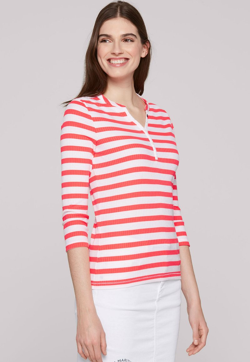 Red and white striped long-sleeve top with a Henley neckline and ribbed texture, paired with a white skirt featuring embroidered detail.