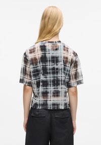 Camicia a maniche corte in tessuto trasparente a quadri. Presenta un motivo a griglia con colori scuri e chiari. Vestibilità rilassata con scollatura rotonda.