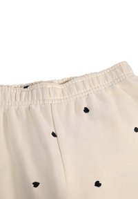 Pantalones de cintura elástica beige con pequeños patrones de corazones negros, hechos de una tela suave con una textura lisa.